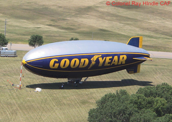 The Goodyear GZ‑20A “Spirit of Goodyear” moored on the Pioneer Airport field north of the historic hangars, photographed from the Bell 47G during AirVenture 2007. The blimp operated from the Pioneer grass strip throughout the show, supported by a compact ground crew and mobile mooring mast. This elevated view captures the classic mid‑2000s Pioneer layout, with the blimp positioned on the north side of the campus rather than the main Wittman mooring area.