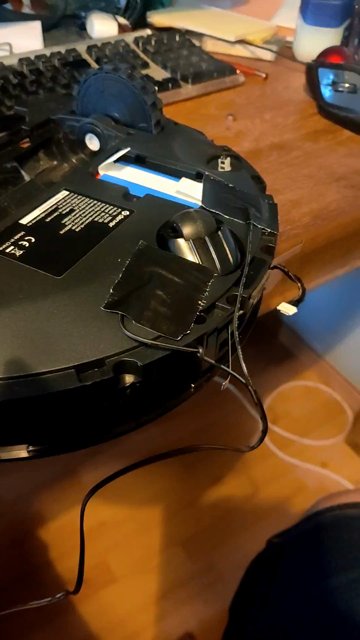 Robot vacuum cleaner lying on its back, partly taken apart. It's says 'charging' and is lifted up to show it lights up green to indicate charging.