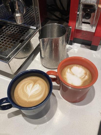 2 lattes, side-by-side, one with a pleasant heart-shape design from the poured milk, the other one considerably more messy.