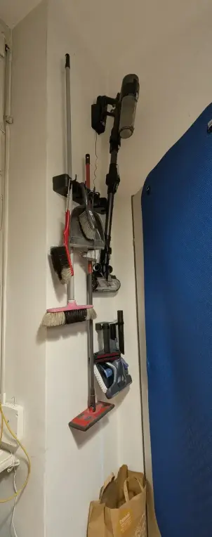 a small corner in a flat behind a door. Several cleaning supplies are orderly hung on the wall. In order to hang the vacuum and it's tools this way, 3d printed parts had to be designed.