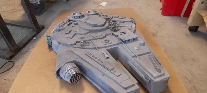 Scratchbuilt cardboard model of a spaceship type of vehicle on the floor. Painted mainly with base gray. Inspired by the Millennium Falcon.
