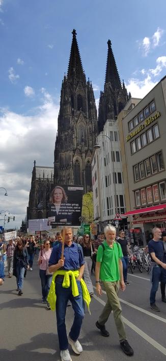 Demonstranten halten vor dem Kölner Dom ein Transparent mit dem Bild der Wissenschaftlerin Claudia Kemfert und ihrer Frage: "Warum wird immer gefragt, was Klimaschutz kostet, statt zu fragen, was es uns kostet, wenn wir nichts tun?"