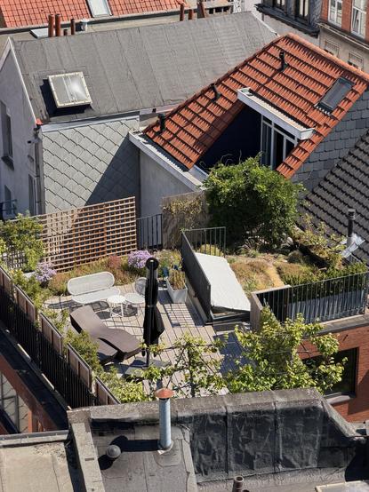 Zoomed in photo of a nice rooftop garden, with nice benches and lots of plants, and a closed umbrella.
