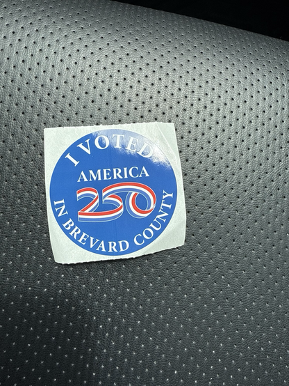 Round sticker with a blue background and white font "I Voted in Brevard County", and in the center the word America and 250 spelled in red white and blue ribbon font.