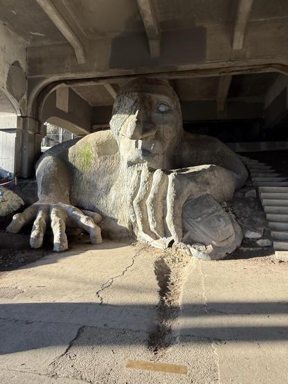 The Fremont Troll, made of concrete and dragging a VW Beetle towards it, under the Fremont Bridge