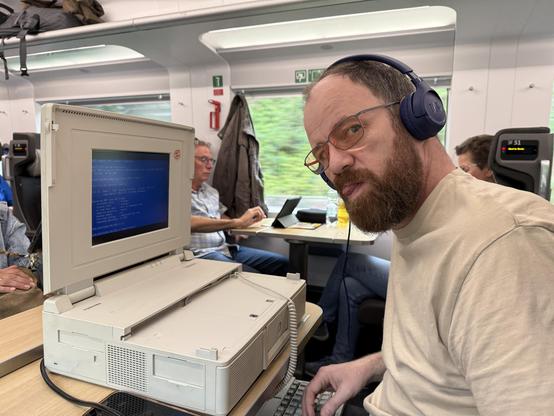 Me on the train preparing the Toshiba. Big honkin' machine on the table, silly blue headphones on my head.
