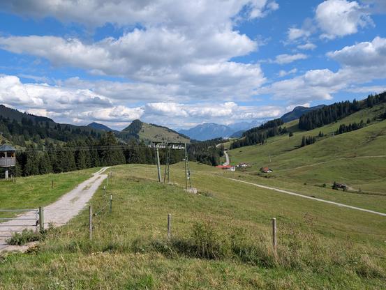 Blick vom Sudelfeld Richtung Kaisergebirge unter weiß-blauem Himmel.