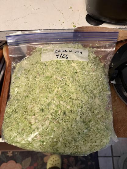 A picture of the resulting light-green chopped slaw thrown into a gallon freezer bag, sitting on my cutting board next to my white laminate counter with the corner of the food processor in view and one of the ugliest Crocs known to humankind (neon yellow ) out of focus on the floor. Sorry, those are my house shoes because they are washable. Having pets requires having washable house shoes.