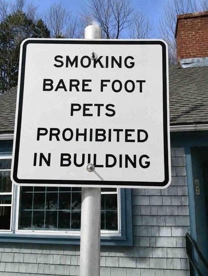 Photo. A sign in front of a building. It reads, “Smoking barefoot pets prohibited in building”