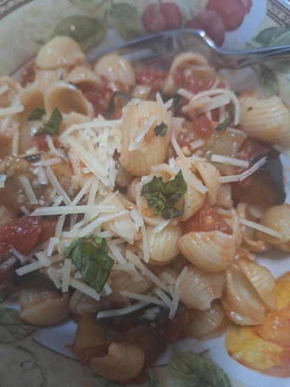 Shell pasta with diced eggplant, tomatoes, garlic, basil, and parmesan Romano cheese sprinkled over. A little of the eggplant skin shows it's darkened purple skin on the right. Eggplant and basil are from our garden.