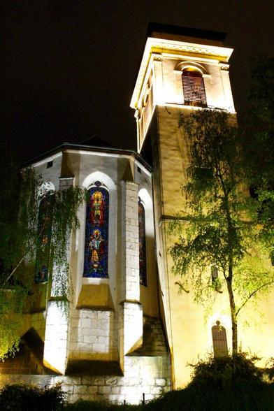 Nachtaufnahme einer kleinen, beleuchteten Kirche mit einem Buntglasfenster