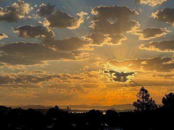 early morning sun over the bay and richmond bridge, obscured by scattered clouds creating crepuscular rays. in the distance mt diablo can be seen.
