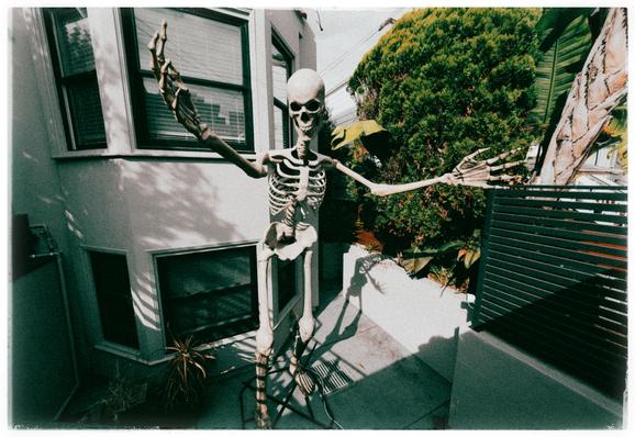 Yes yes, it's that time of year. The neighbors have set out a giant 12-foot skeleton in their front yard. The skeleton stands on a concrete patio in front of their homes bay windows. With a toothy smile on its face and arms outstretched, it looks ready to hug passersby like a bony nona ready to greet her grandchildren who don't visit often enough.