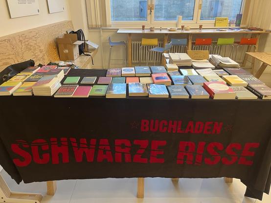 Büchertisch mit vielen Büchern und einem Banner mit der Aufschrift "Buchladen Schwarze Risse"