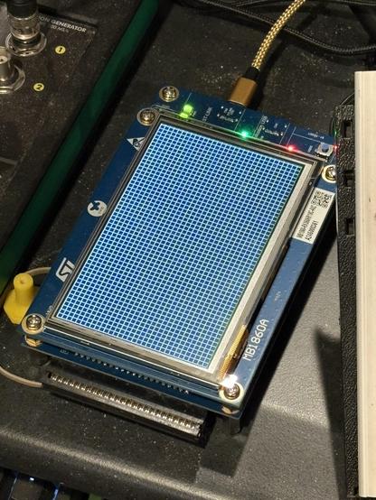 And ST32U5G9Z-DK2 Development board showing a grid pattern on the attached LCD.