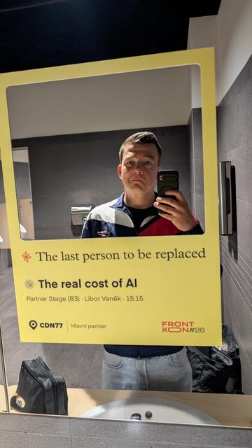 Me standing in front of the mirror in the toilet at the conference location. They put a frame on the mirror with your face at the center. Below it says "the last person to be replaced" making promo for a talk later today titled "the real cost of ai"