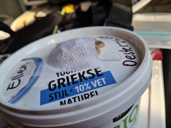In het deksel van een grote yoghurtpot zit een rond gat met witte, doorschijnende tape eroverheen, dat bol staat. Aan één kant duwt een klein oesterzwammetje het tape omhoog