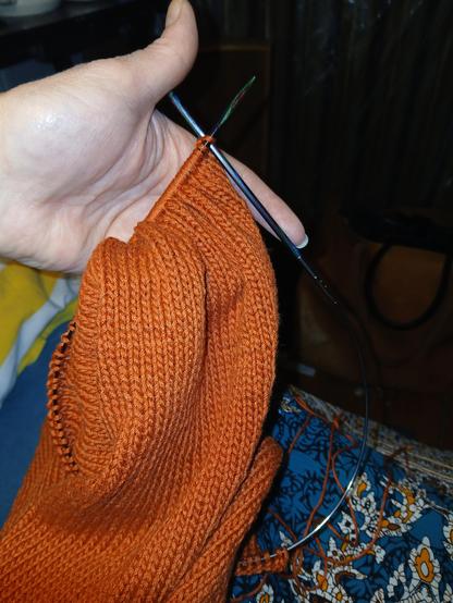 sleeve of a dark orange handknit sweater still on the needles held up by the left hand.