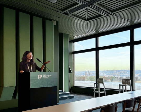 Elena standing at a podium with scenic views of Prague out the window.