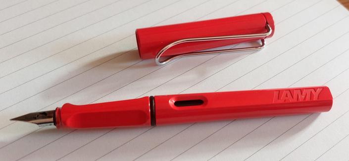 A red Lamy Safari fountain pen and its cap, resting on a piece of lined paper.