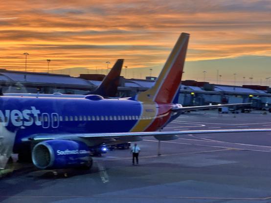 bright orange clouds reflect the setting sun at an airport departure gate. In the foreground is part of a Southwest 737.