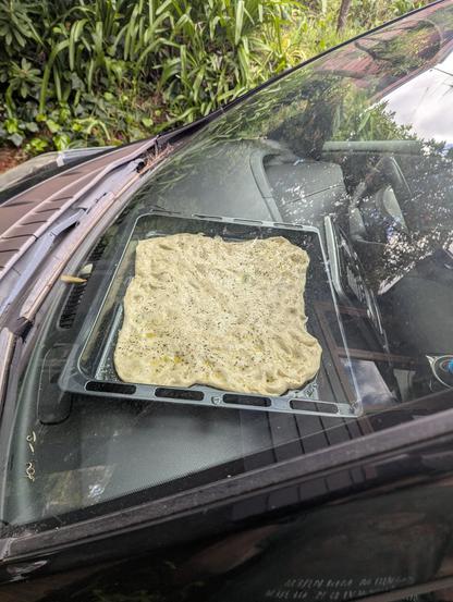 Focaccia on a tray sitting on the dashboard of our black Nissan Leaf.. it's warm and sunny