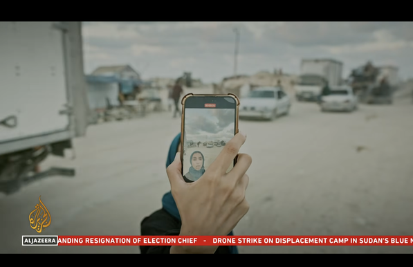 screenshot al jazeera. show woman hold self phone - her hand holding the phone and her face visible on the screen.