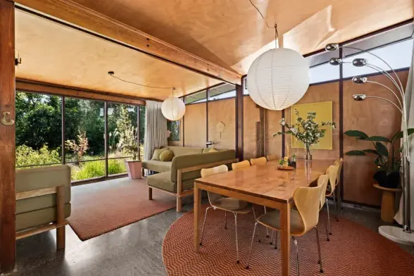 Listing photo 4 from 806A Gordon Road, Raureka, Hastings.

The dining and living areas of a renovated post-and-beam house, with floor-to-ceiling windows along one wall, paneled wood and clerestory windows along the other walls, paneled wood ceiling, and concrete floor.
