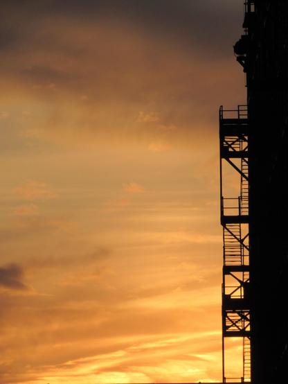 A fiery sky at dawn provides the background of a fire escape on the side of a building. No need to escape this fire.