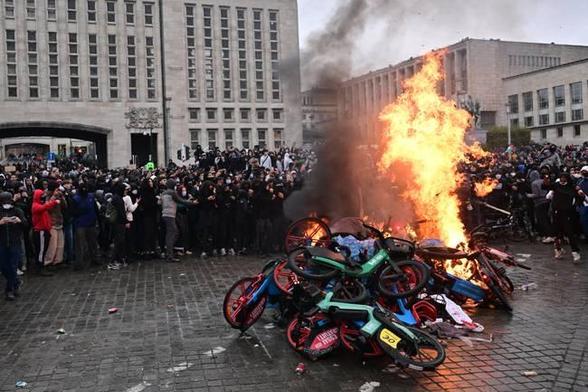 A pile of commercial e-bikes set on fire with a crowd watching