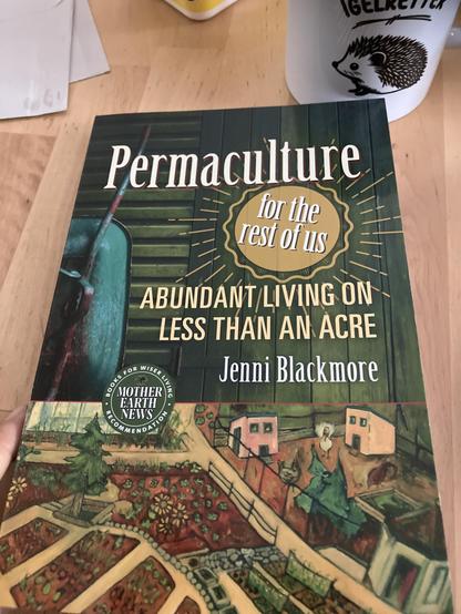 Ein Buch liegt auf einem Holztisch. Der Titel ist: „Permaculture for the rest of us“ von Jenni Blackmore