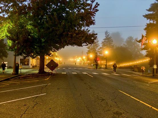 Downtown Snohomish at dawn in the fog, string lights and street lamps glowing, a few runners crossing the empty street.