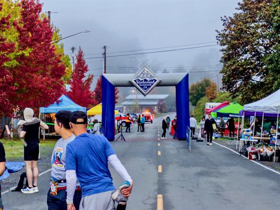 The Snohomish Running Co arch on a foggy grey morning, red autumn trees on the left, runners warming up in front of it.