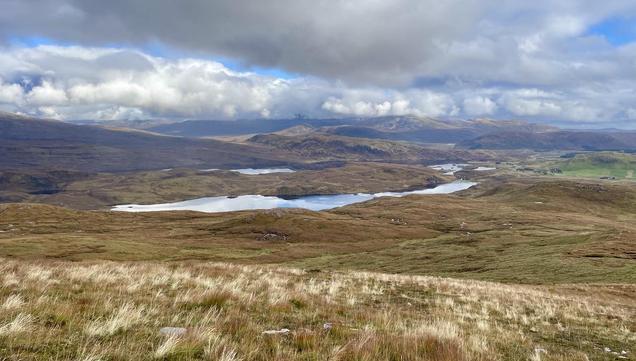 A photo of an expanse of wet moorland in rich autumn colours, with lochs lochans & hills