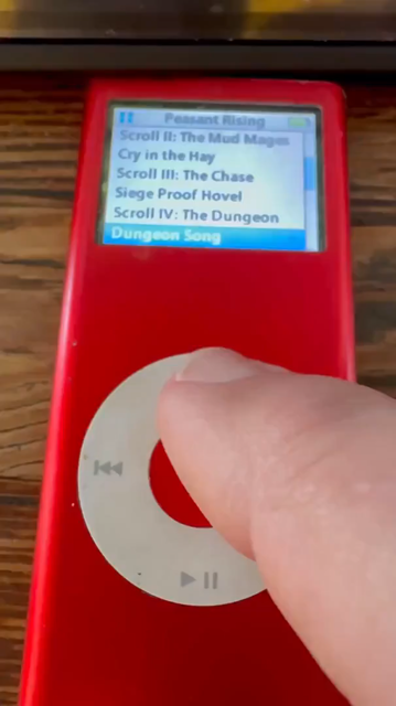 A hand scrolling through the ui of an old red ipod mini that is playign an album called Peasant Rising by Netherwilds. The music starts off sort of medieval folk sounding, but then the drums and guitars come in and it's all metal. The camera zooms out to show an ipad screen above the ipod. Art on the screen says the words "Good (Smart)" on it, as if in approval of the music playing on the ipod.