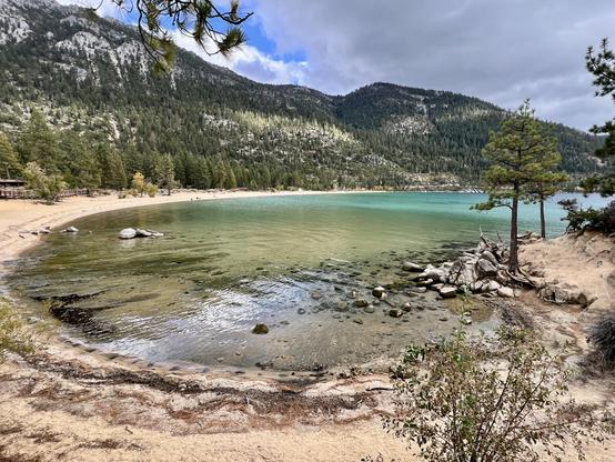 A bay in a lake. A sandy beach around a shallow bay. Mountains in the background.