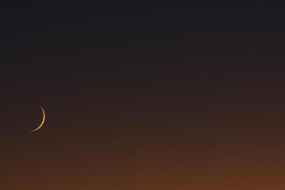 The moon and Mercury (upper right corner) hang in the evening twilight sky. The sky is orange-pink at the bottom of the frame and transitions to blue at the top.