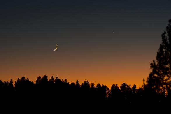 With a wider view, but still telephoto, the sky gradient of color is even stronger and larger. Foreground trees are dark silhouettes.