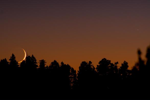 The moon is setting behind the ridge covered with conifers. Mercury is still above the tree line.
