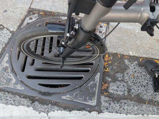 A shot of the same storm drain cover with my front bicycle wheel on it, showing how the slots can swallow the width of the wheel.  (And mine isn't even as svelte as many other types of road bikes out there.)