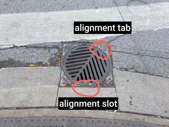 A marked-up version of the first photo with the words "alignment tab" aimed at a red circle around the top left corner of the circular storm drain cover, and "alignment slot" in the bottom dead center of the square frame where the cover should be aligned.