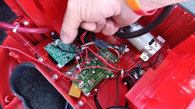 Two circuit board inside a red housing. A hand is holding a detached black wire with some corrosion on the free end. Matching corrosion on the PCB. Other end leads to a metal compressor motor housing.