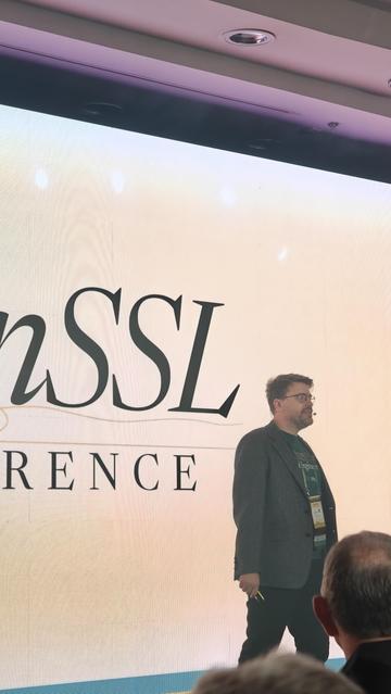 Anton in front of a huge video wall displaying the OpenSSL Conference logo