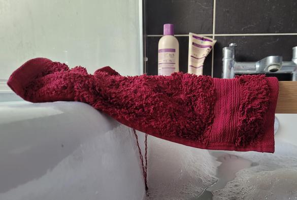 A flannel above a bath on a bath shelf with long strings of thread hanging down off it.
