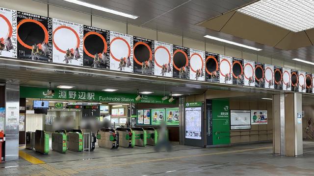 A row of launch posters runs all the way along the wall above the train station ticket gates.