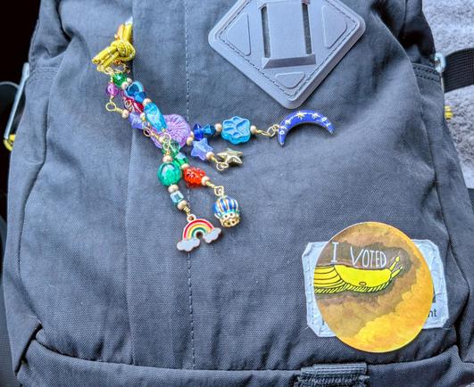 A black purse with a beaded dangly decoration and an I voted sticker with a banana slug.