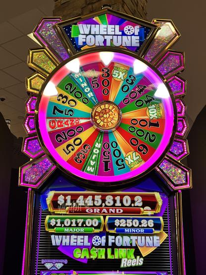 A slot machine with a name on top saying Wheel of Fortune. It is bright and colorful and designed to catch the attention of passers-by.