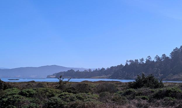 Humboldt Bay in the distance taken from the road to the beach. The sky and the bay are blue.