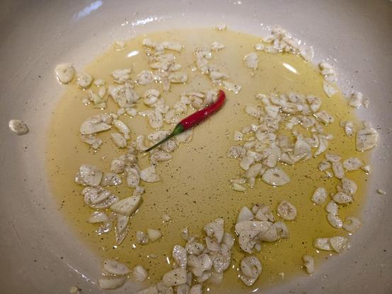 A small Thai red pepper in a pan with sliced garlic and olive oil.
