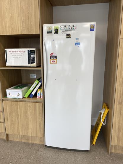 A fridge and microwave in a work kitchenette. There’s a label on the fridge that looks like an efficiency label.